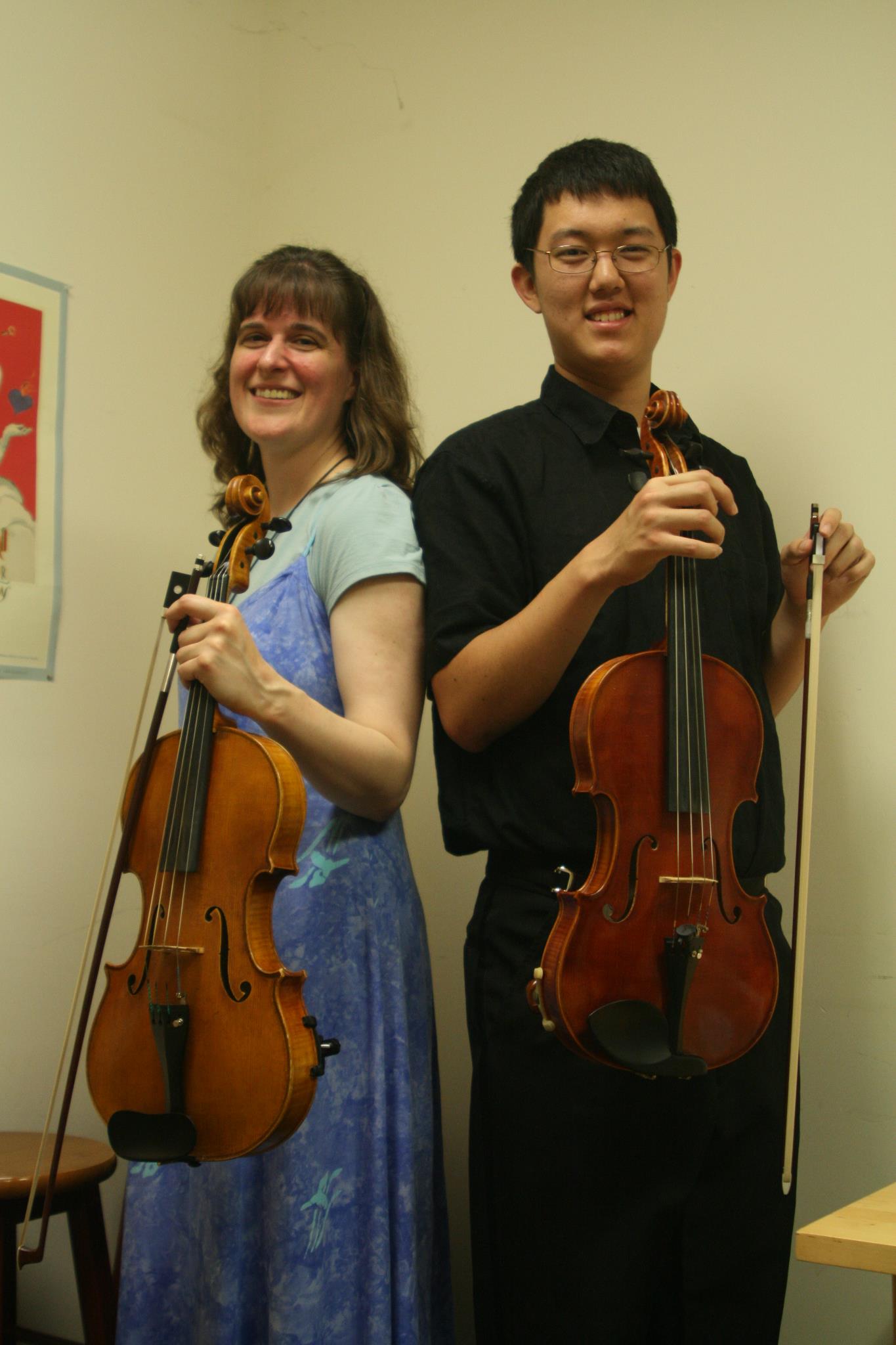Leah in blue dress holding a viola back to back with Dan in black holding a viola with a white background