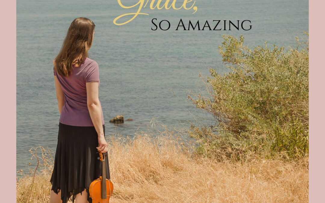 Leah Irby standing in grass overlooking the ocean, looking into the sea while holding her viola.