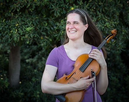 Leah Irby wearing a purple top standing in front of trees, holding her viola