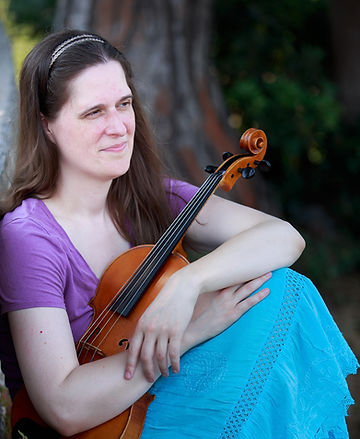 Leah Irby sitting with her viola, wearing a purple top and turquoise skirt, with blurry trees in the background.