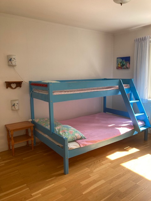 Bunk bed with pink sheets and blue paint in a sunny room. There are blue and white pin stripe curtains on the window and there are two wall lamps with frogs dancing and matching blue and white pin stripes